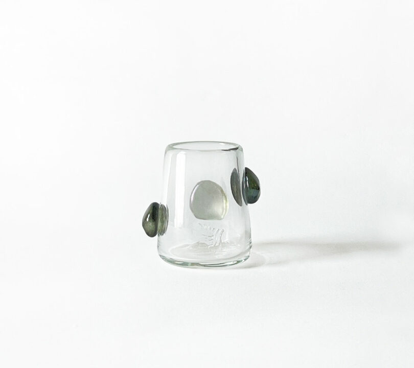 A clear glass tumbler by Jess Humphrey with three attached black stones placed asymmetrically.