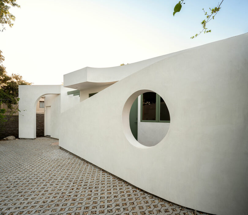 Modern white building with a geometric design featuring a circular window and patterned ground in front.