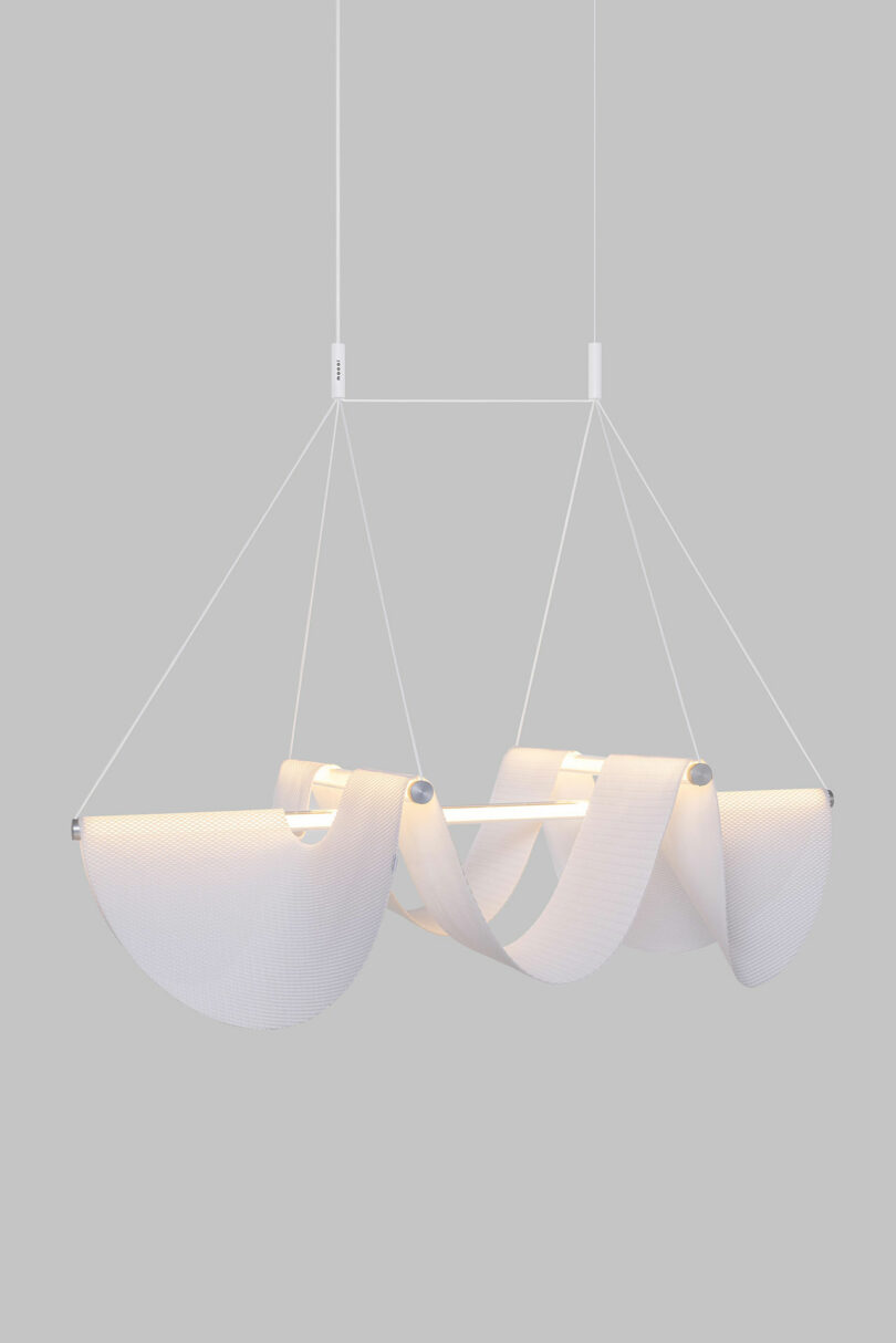 The Drape Light by Jamie Wolfond with a wavy fabric design suspended by four thin wires against a gray background.