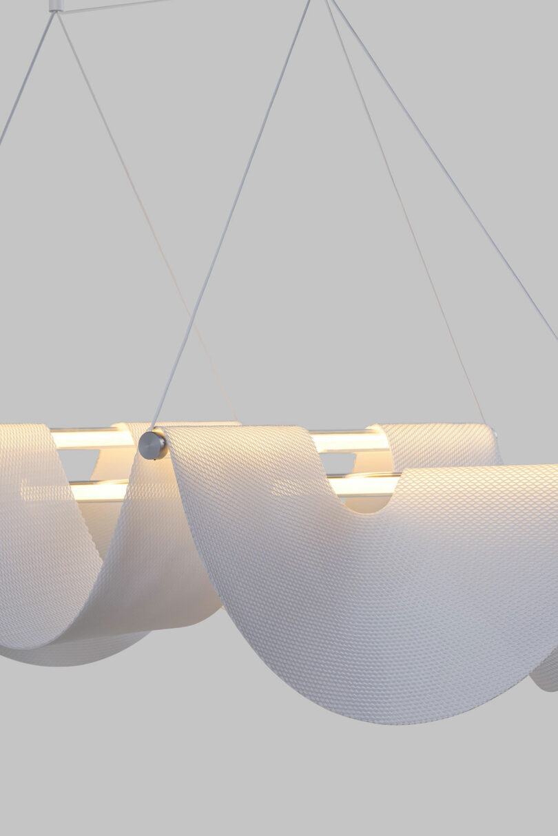 The Drape Light by Jamie Wolfond, featuring wave-like, textured shades hangs from thin wires against a plain background.