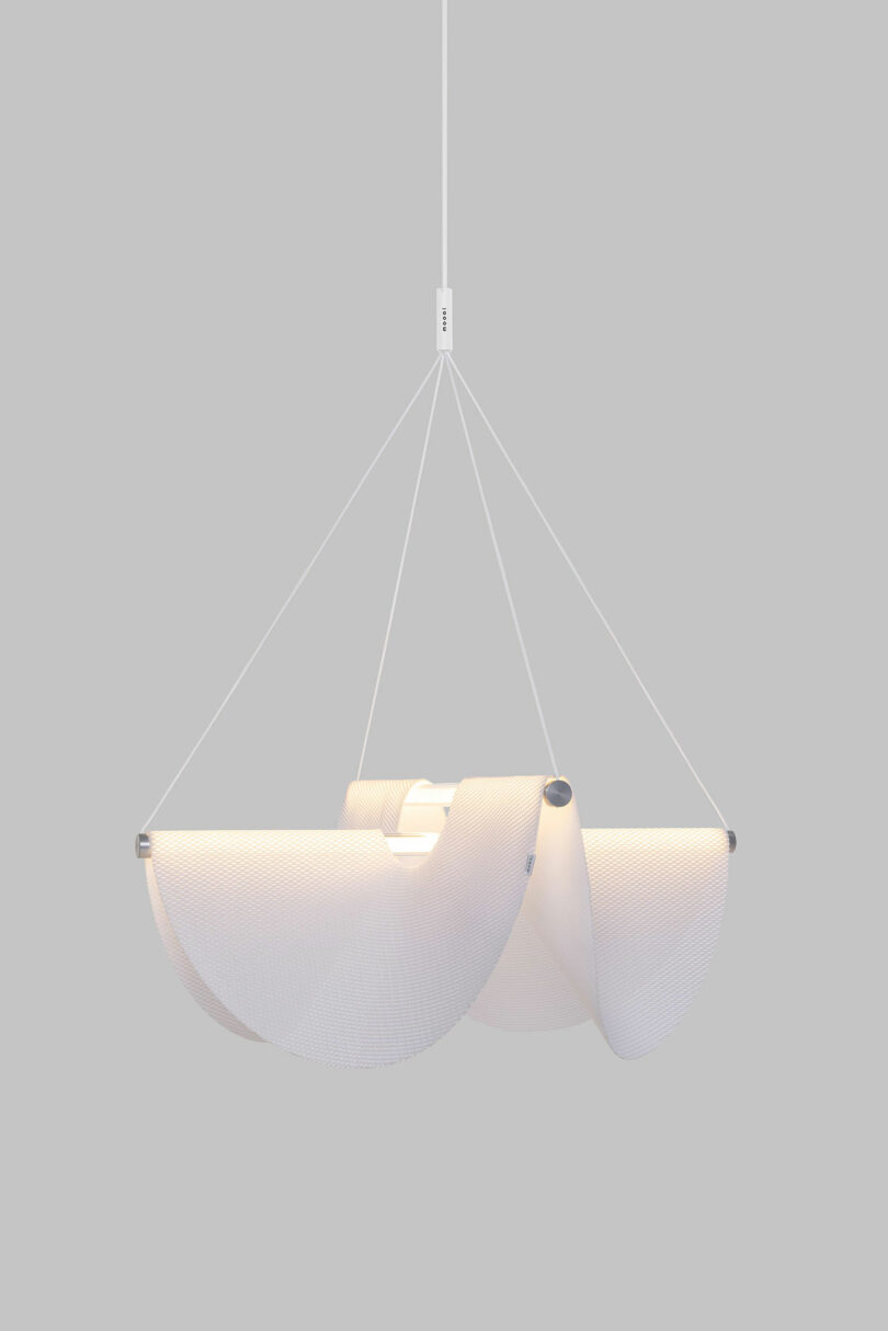 The Drape Light by Jamie Wolfond with a spherical bulb, surrounded by a contemporary wavy, white fabric design, suspended by four wires from a central cord.