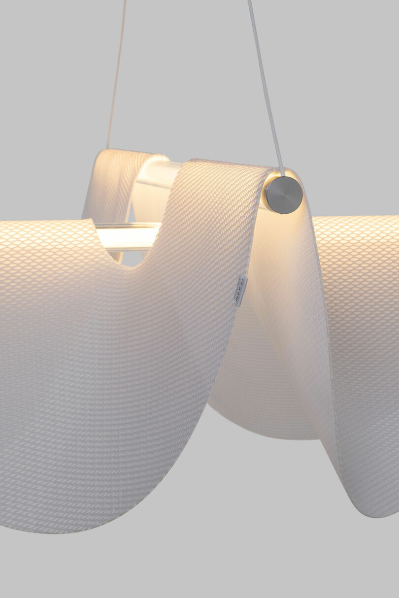 Close-up of the Drape Light by Jamie Wolfond with a sleek, white, wavy design, emitting a soft glow. The material has a textured, mesh-like appearance.
