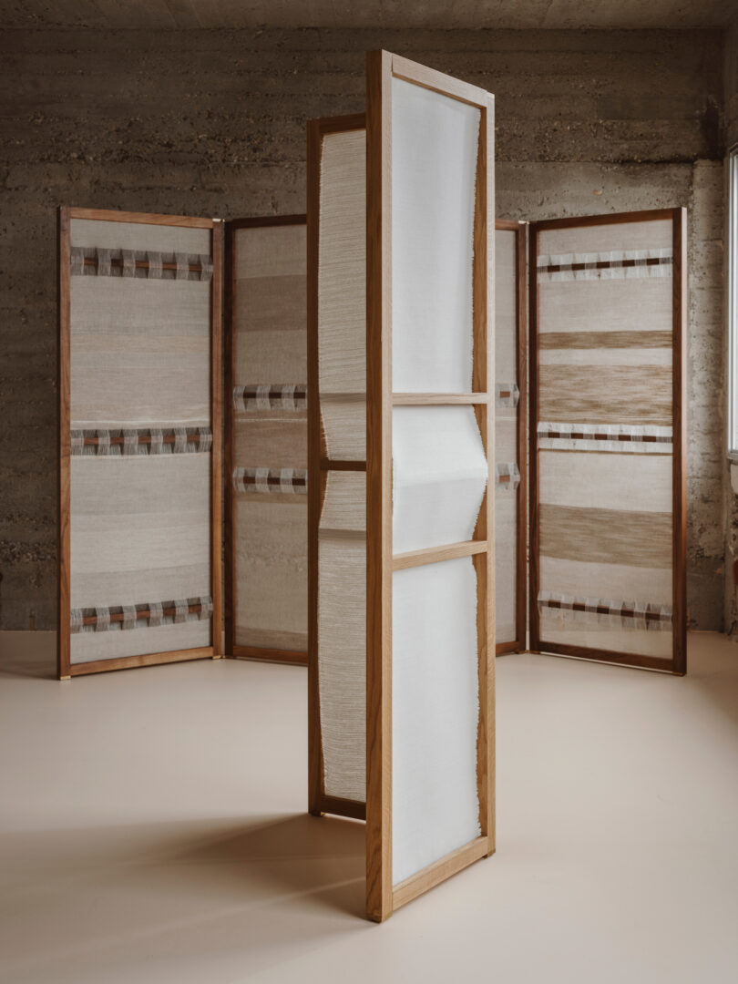 A room divider made of wooden frames and textile panels stands in an industrial-style room with concrete walls