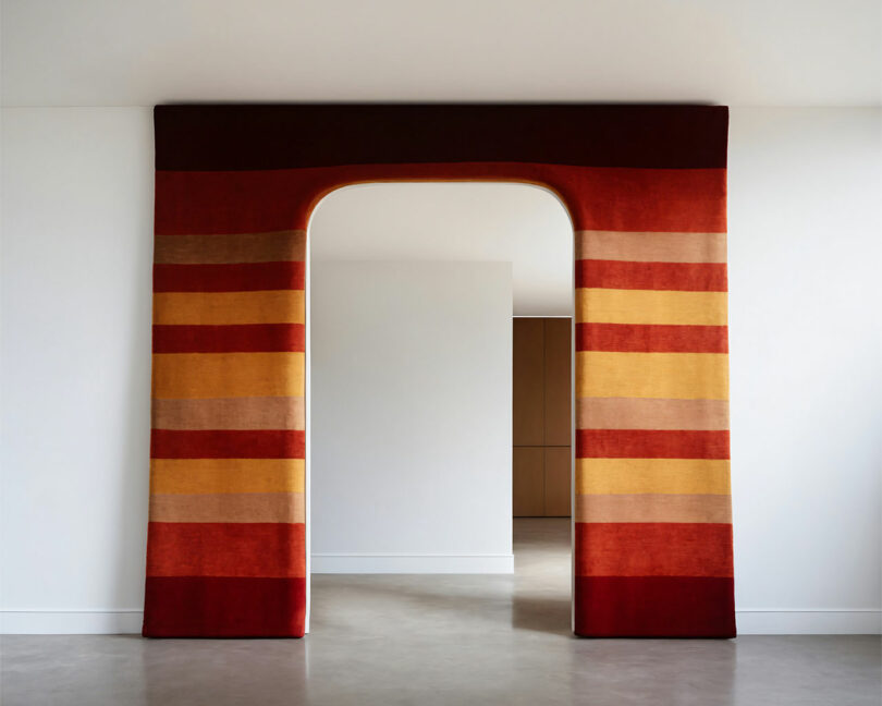 A doorway framed by a colorful, striped fabric covering in shades of red, orange, and yellow, within a minimalist interior space.