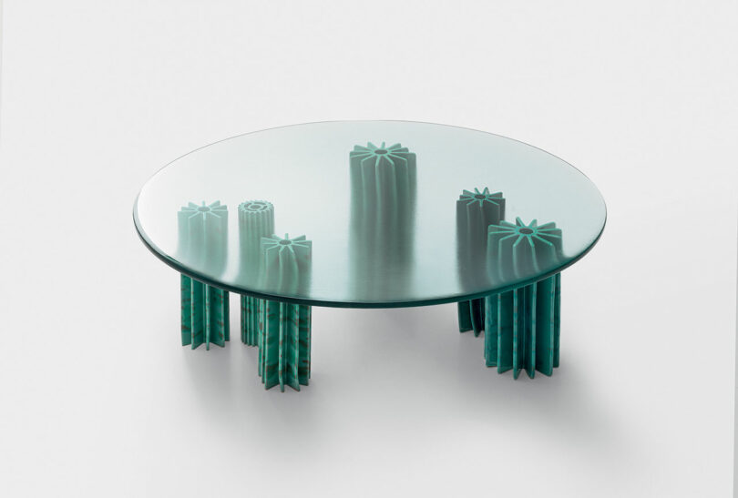 A round glass coffee table, Helico by Nicolò Morales for Paola Lenti, with multiple teal, intricately carved pillar legs of varying heights forming the base.