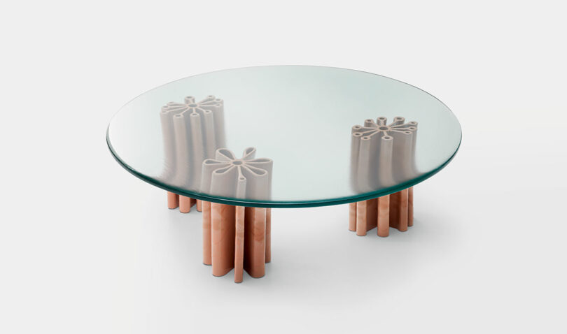 A full shot of Primula by Nicolò Morales for Paola Lenti, a round glass coffee table with four decorative pink ceramic legs arranged in a floral pattern.