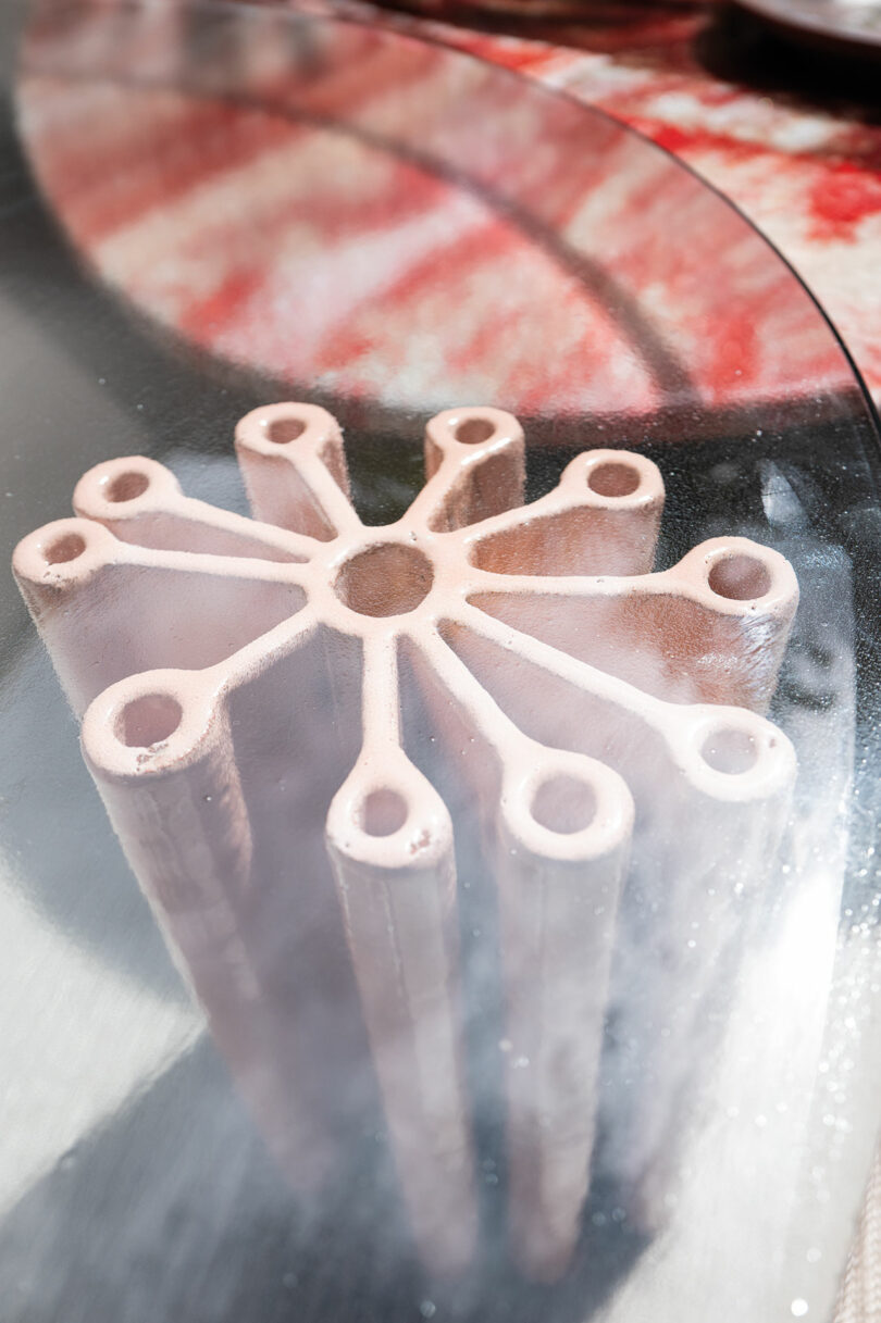 A close-up view of Primula by Nicolò Morales for Paola Lenti, a geometric sculpture with a circular design, made up of interconnected raised cylindrical structures, viewed through a glass surface.