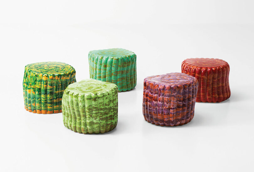 Five colorful ceramic stools with ridged, cylindrical shapes are placed against a plain white background. Named Anemone by Nicolò Morales for Paola Lenti, the stools are variously colored with green, orange, purple, and red tones.