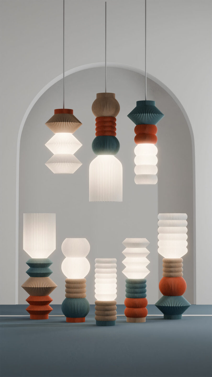 Nine modern pendant and table lamps, including the innovative STAK Modular Lamp, showcase pleated designs in various shapes and colors like white, blue, brown, and orange against an arched backdrop.